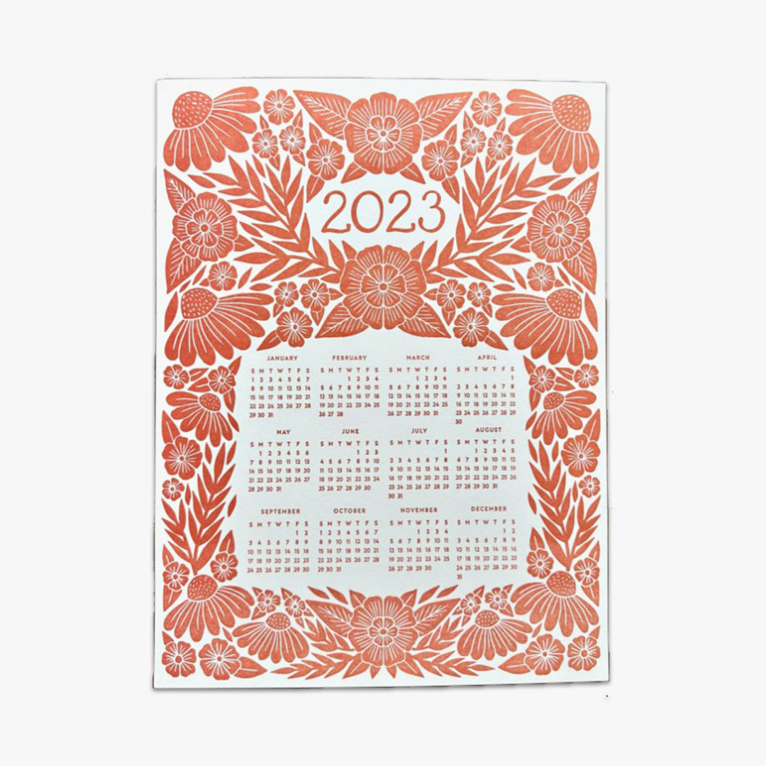 Our Red Floral Letterpress 2023 Calendar showcases a detailed floral graphic design that's letterpress printed with red ink on a thick museum, off-white board. The number 2023 is the headline on the upper third of the page, and the annual calendar (January through December,) is featured on the mid and lower third of the page. The 2023 calendar and 2023 headline are both surrounded by the floral graphic design. This photo shows the entire one-page calendar.