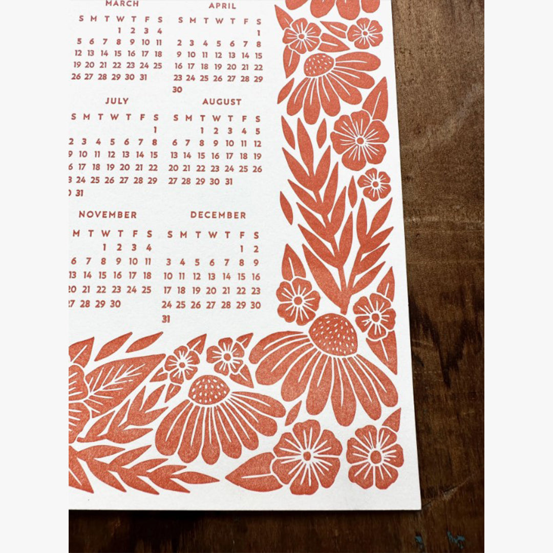 Our Red Floral Letterpress 2023 Calendar showcases a detailed floral graphic design that's letterpress printed with red ink on a thick museum, off-white board. The number 2023 is the headline on the upper third of the page, and the annual calendar (January through December,) is featured on the mid and lower third of the page. The 2023 calendar and 2023 headline are both surrounded by the floral graphic design. This photo shows a close-up of the bottom right section of the one-page calendar.